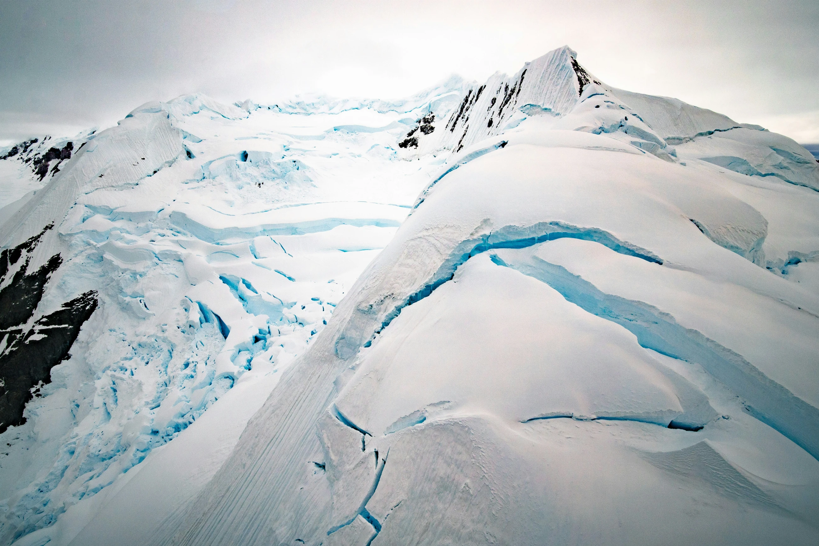Aerial shot from helicopter over mountains near Paradise Bay, Antarctica.  Incredible, dramatic and deep crevasses illuminated with icy blue light from within. | © Unsplash / Rod Long